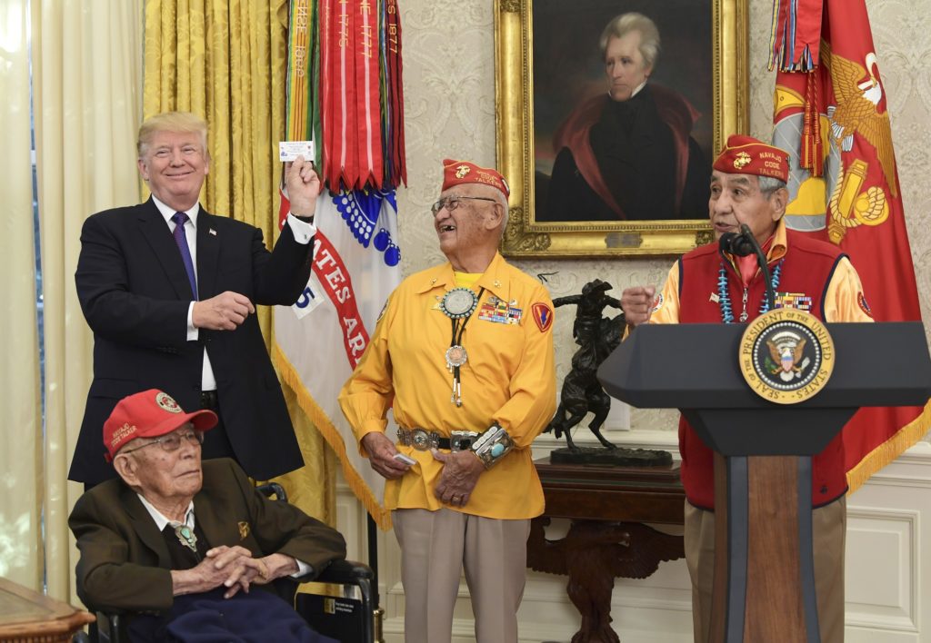 President Donald Trump, standing left, holds up the card of Navajo Code Talker Thomas Begay, center, during their meeting in the Oval Office of the White House in Washington, Monday, Nov. 27, 2017. Navajo Code Talkers Fleming Begaye Sr., seated, Peter MacDonald speaks at right. (AP Photo/Susan Walsh)