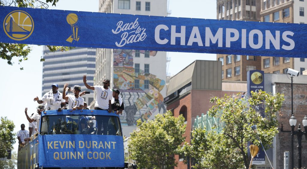A champions banner is placed overhead as a bus carrying Golden State Warriors' Kevin Durant and Quinn Cook rides down the route during the team's NBA basketball championship parade, Tuesday, June 12, 2018, in Oakland, Calif. (AP Photo/Tony Avelar)